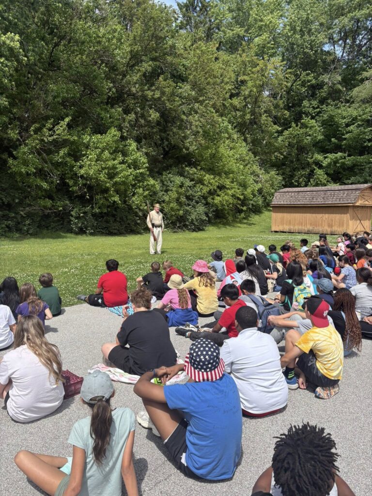 5th grade students sitting outside and listening to a presentation from Mr. Caddell about the Civil War.