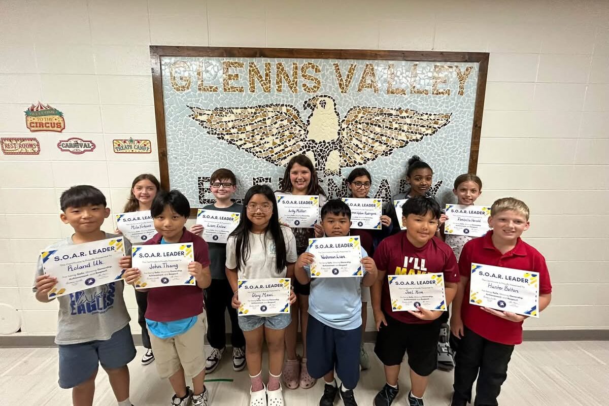photo of twelve fifth grade students standing in front of a tile mosaic of an eagle. Students are holding their Soaring eagle award certificate