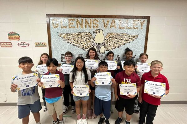 photo of twelve fifth grade students standing in front of a tile mosaic of an eagle. Students are holding their Soaring eagle award certificate
