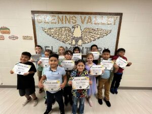 photo of twelve fourth grade students standing in front of a tile mosaic of an eagle. Students are holding their Soaring eagle award certificate
