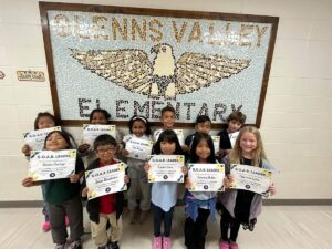 photo of eleven second grade students standing in front of a tile mosaic of an eagle. Students are holding their Soaring eagle award certificate