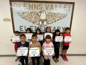 photo of nine third grade students standing in front of a tile mosaic of an eagle. Students are holding their Soaring eagle award certificate