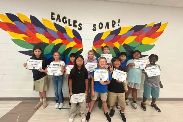 photo of eleven fifth grade students standing in front of the rainbow eagle wings. Students are holding their Soaring eagle certificate