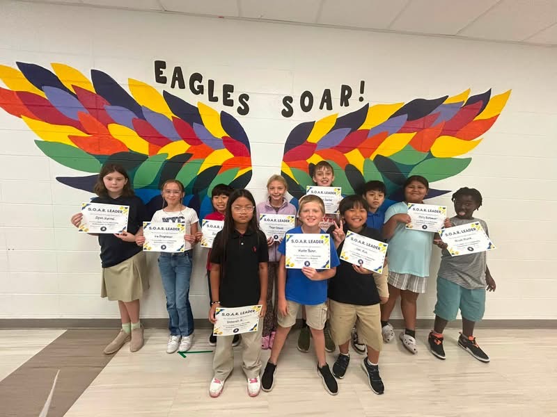 photo of eleven fifth grade students standing in front of the rainbow eagle wings. Students are holding their Soaring eagle certificate