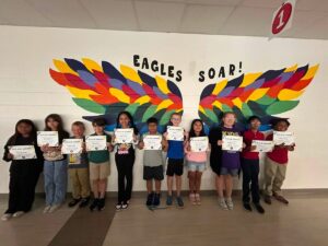 photo of eleven fourth grade students standing in front of the rainbow eagle wings. Students are holding their Soaring eagle certificate