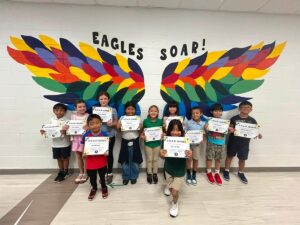 photo of eleven third grade students standing in front of the rainbow eagle wings. Students are holding their Soaring eagle certificate