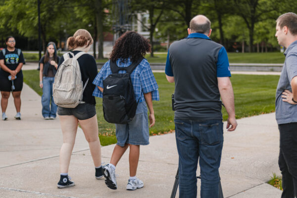 Students walk along a campus sidewalk while members of the filming team prepare and record footage for Perry Township Schools' Innovation & Entrepreneurship Program. Alternative: