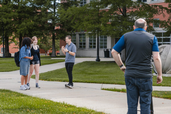 Two students stand on a campus walkway while a videographer gives directions during filming for Perry Township Schools' Innovation & Entrepreneurship Program.