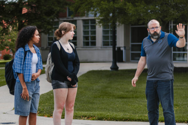 Two students stand on a campus walkway while a videographer gives directions during filming for Perry Township Schools' Innovation & Entrepreneurship Program.